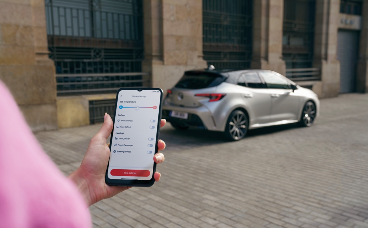 Woman holding phone with MyToyota app open in front of Toyota Corolla Hatchback